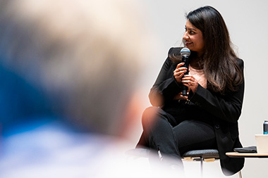 Shruti Kotian, MS 2019 information systems, sitting on a stage and speaking into a microphone at Young Alumni Impact Award ceremony.