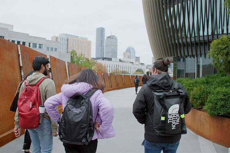 students walking on campus with Boston skyline shown